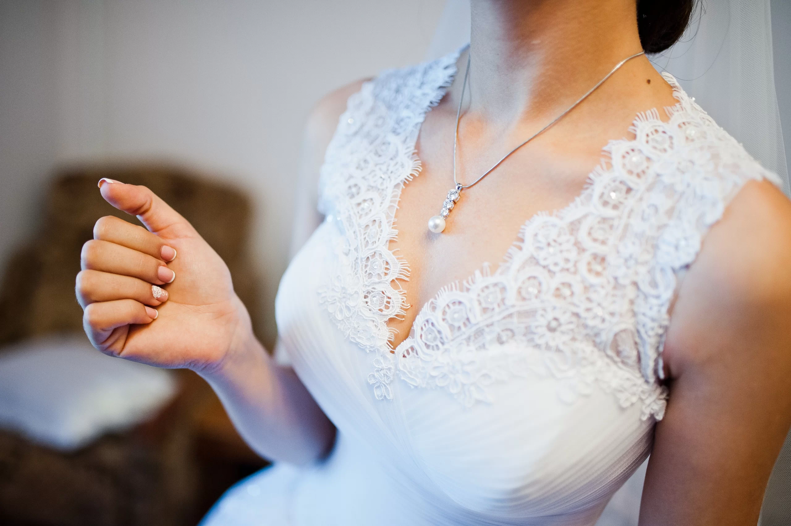 Mulher usando um vestido de noiva branco com um decote V. Ela testá com um colar no pescoço.