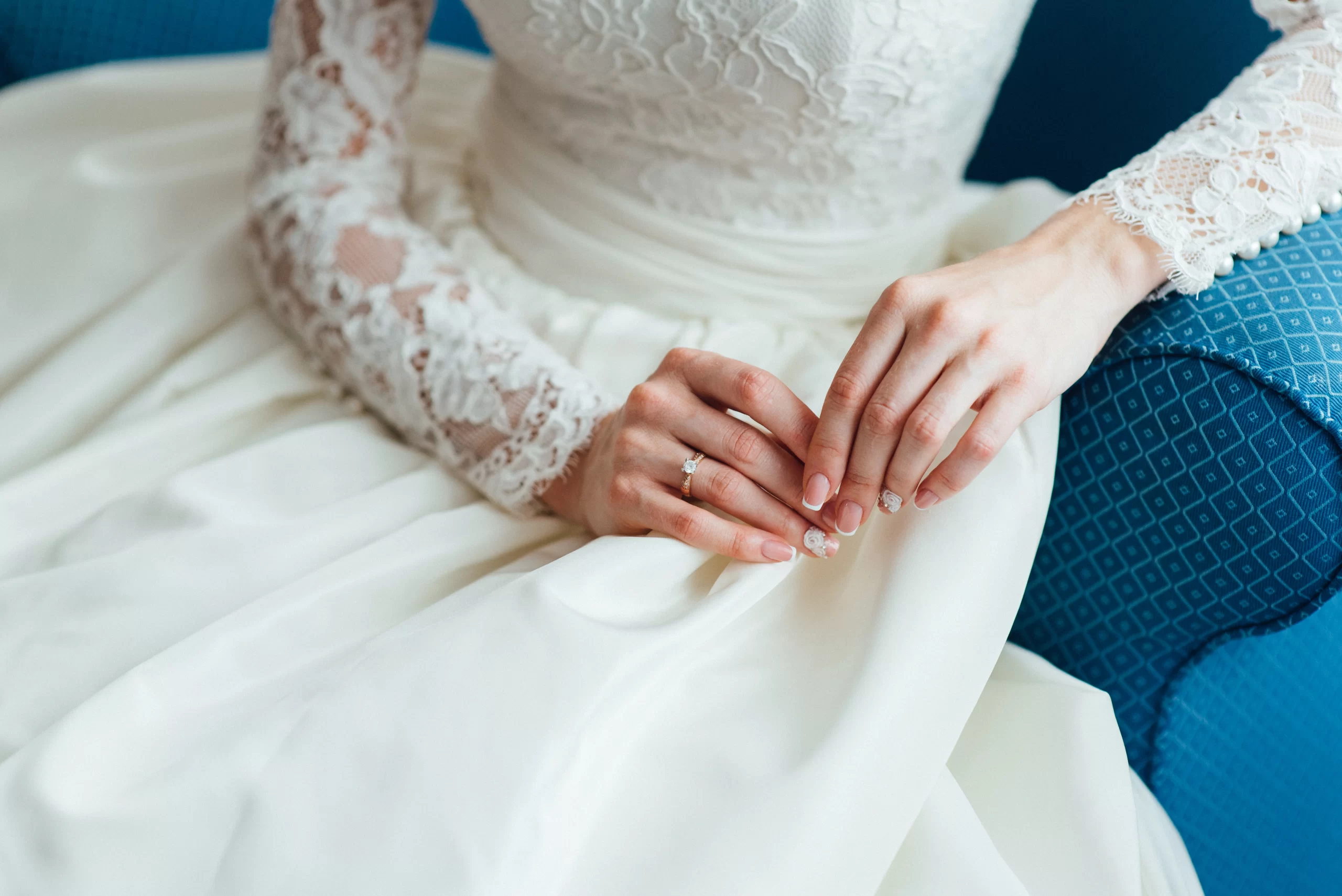 Mulher vestida com vestido de noiva branco. A imagem da foco as mangas compridas e rendadas do vestido.