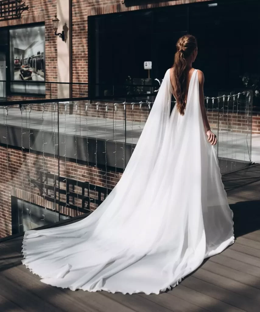 Mulher de costas usando um vestido de noiva branco com capa.