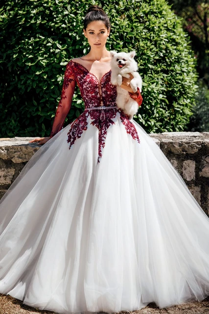 Mulher vestida com um vestido de noiva vermelho e barnco. A mulher segura um cachorrinho no colo.