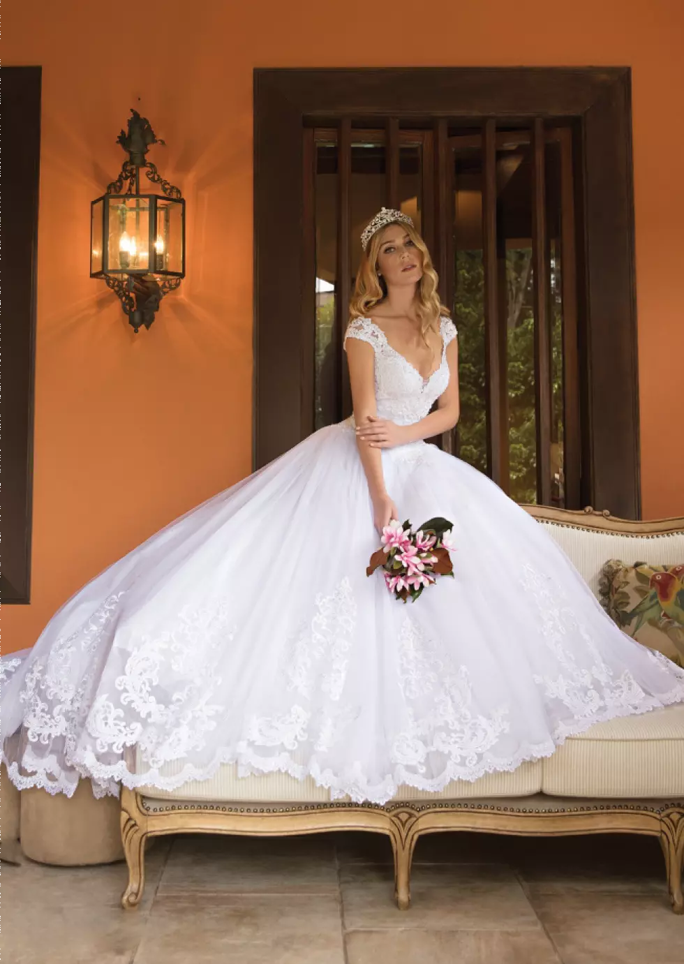 Mulher usando um vestido de noiva branco, ela está fazendo uma pose para a foto e segura um buque de flores com uma das mãos.