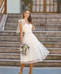 Mulher usando um vestido de noiva para casamento no civil branco. Ela segura um buque de flores brancas em uma das mãos.