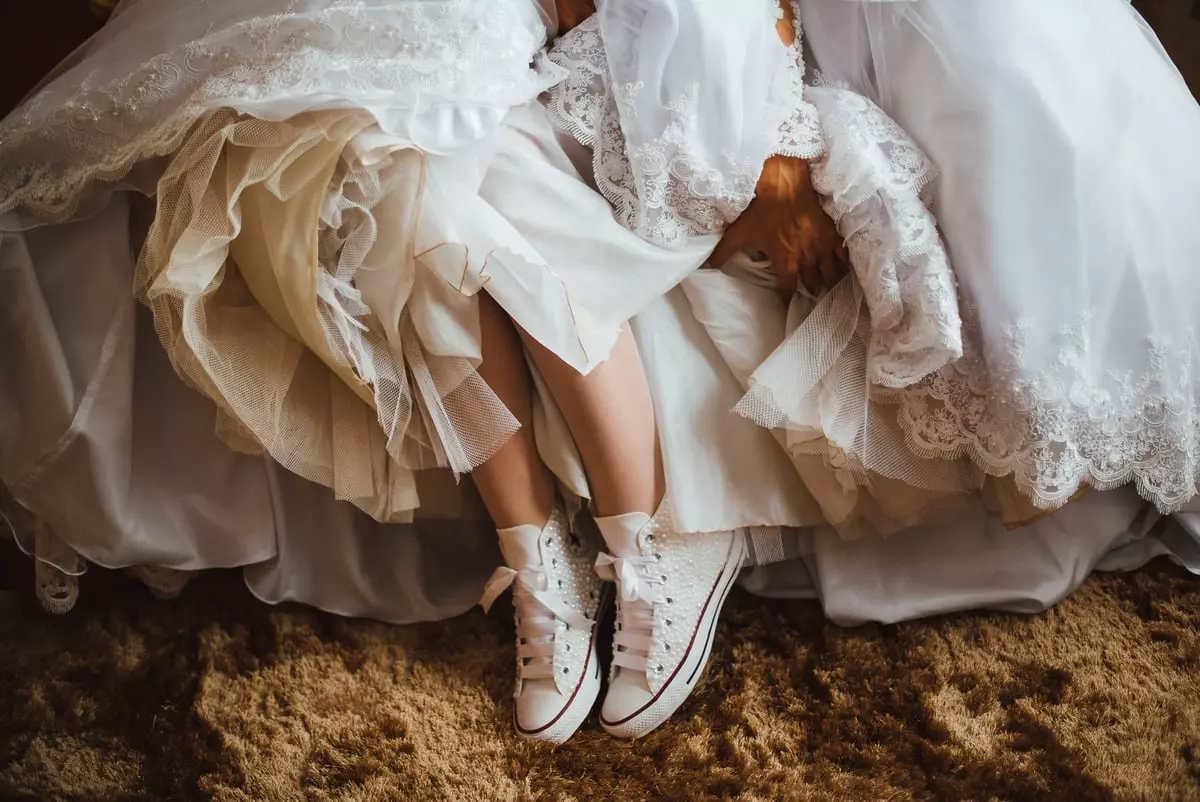 Mulher usando um vestido de noiva branco com alll-star. A foto mostra os pés da mulher com all-star e a barra do vestido.