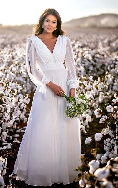 Mulher usando vestido de noiva simples com manga longa. Ela segura um buque de flores nas mãos.