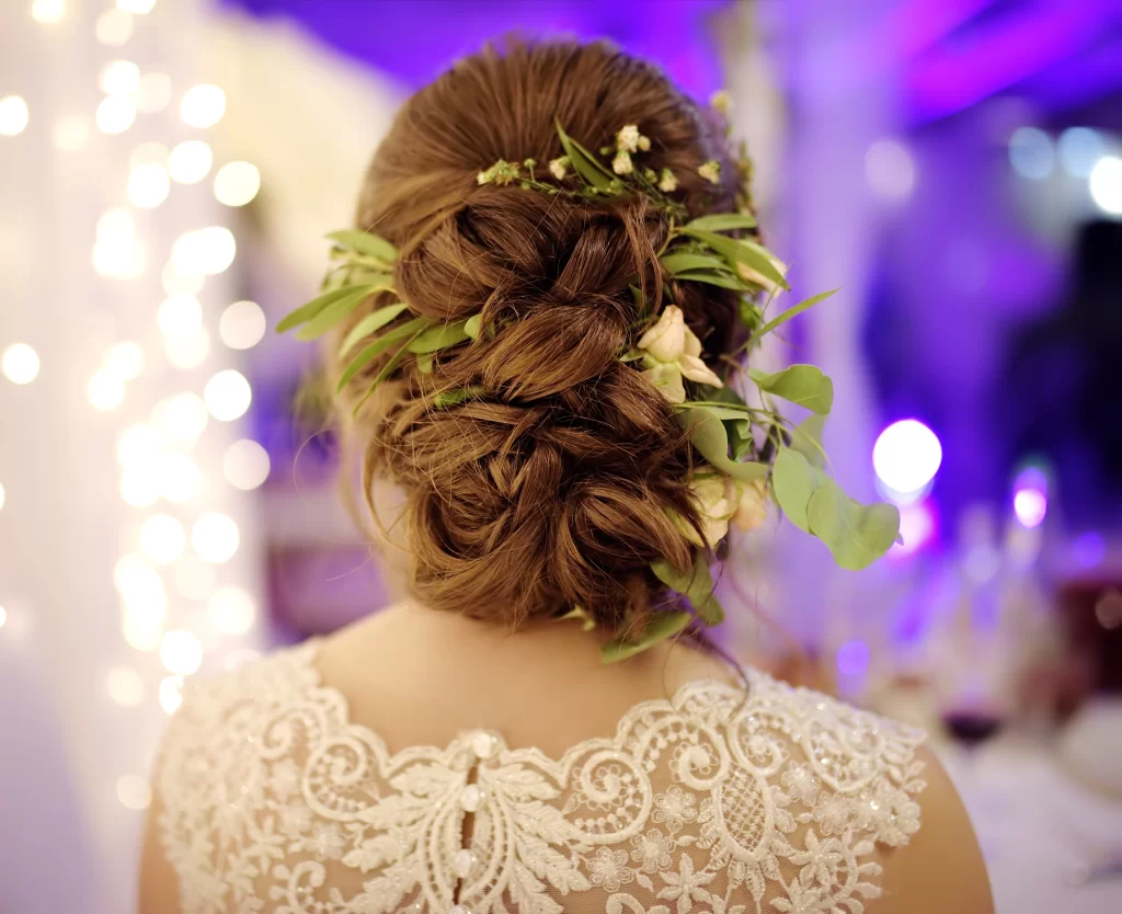 Mulher de cabelos castanhos de costas. Ela usa um penteado com flores e folhas entrelaçadas aos cabelos.