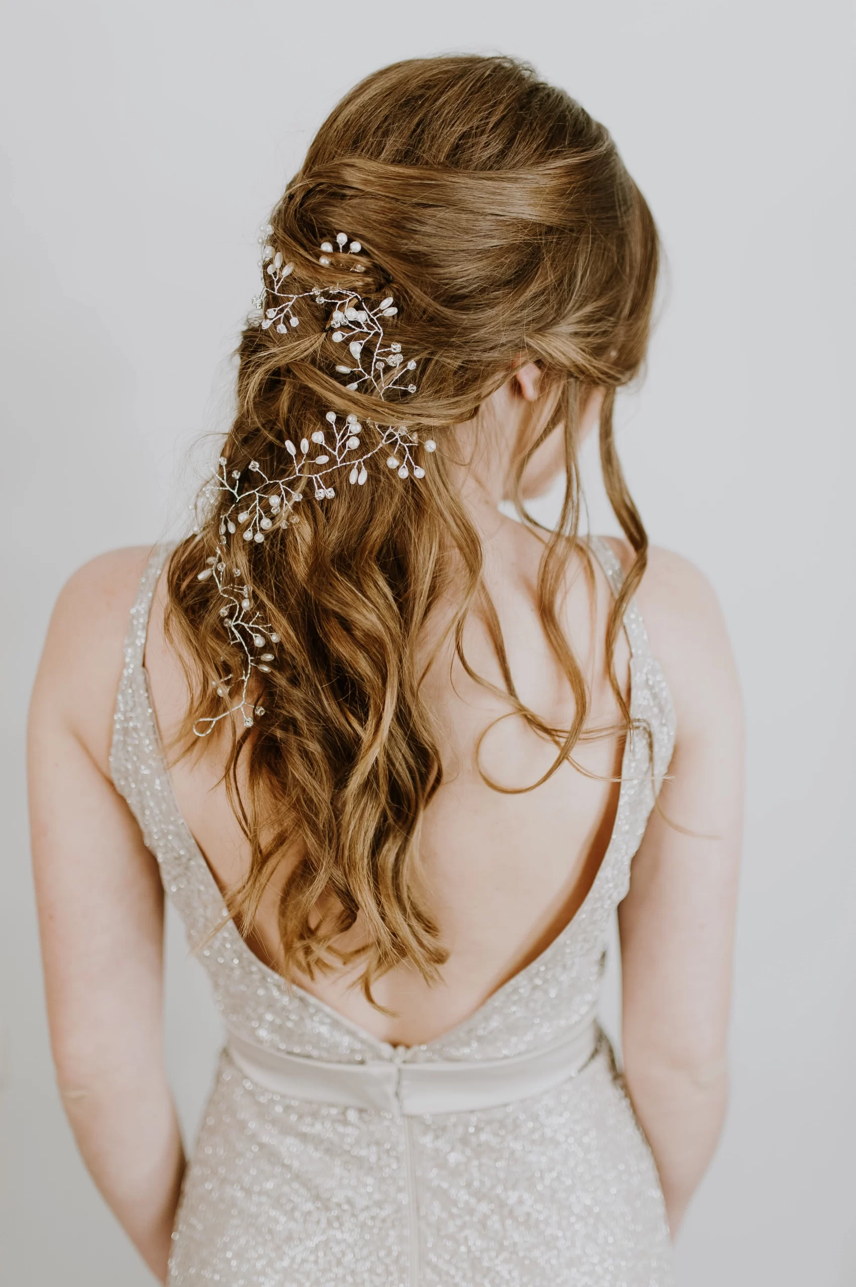 Mulher de cabelos castanho claros de costas. Ela com os cabelos semi-presos com flores brancas atreladas.