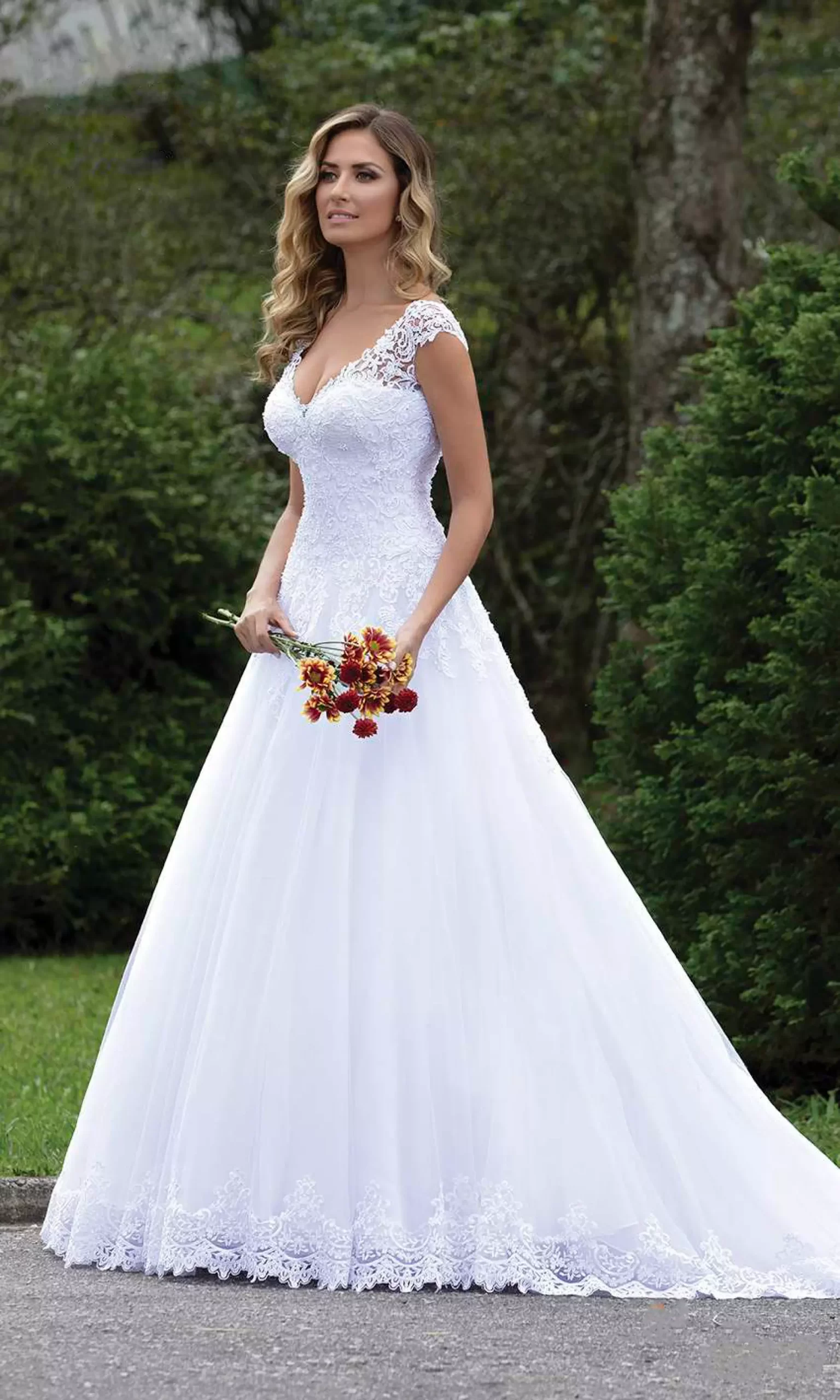 Mulher vestido um vestido de noiva branco evasê. Ela segura um buquê de flores com as mãos.