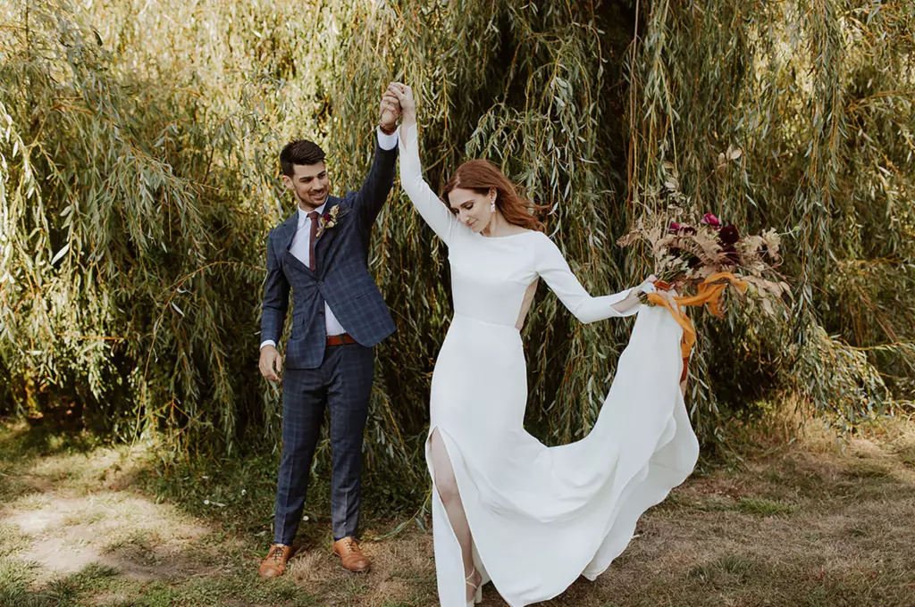 Mulher e homem em uma paisagem campestre. Ele usa um terno preto e ela está usando um vestido de noivas branco simples.