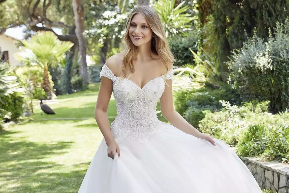 Mulher usando um vestido de noiva branco para casamento no campo com pedrarias na parte de cima do vestido.