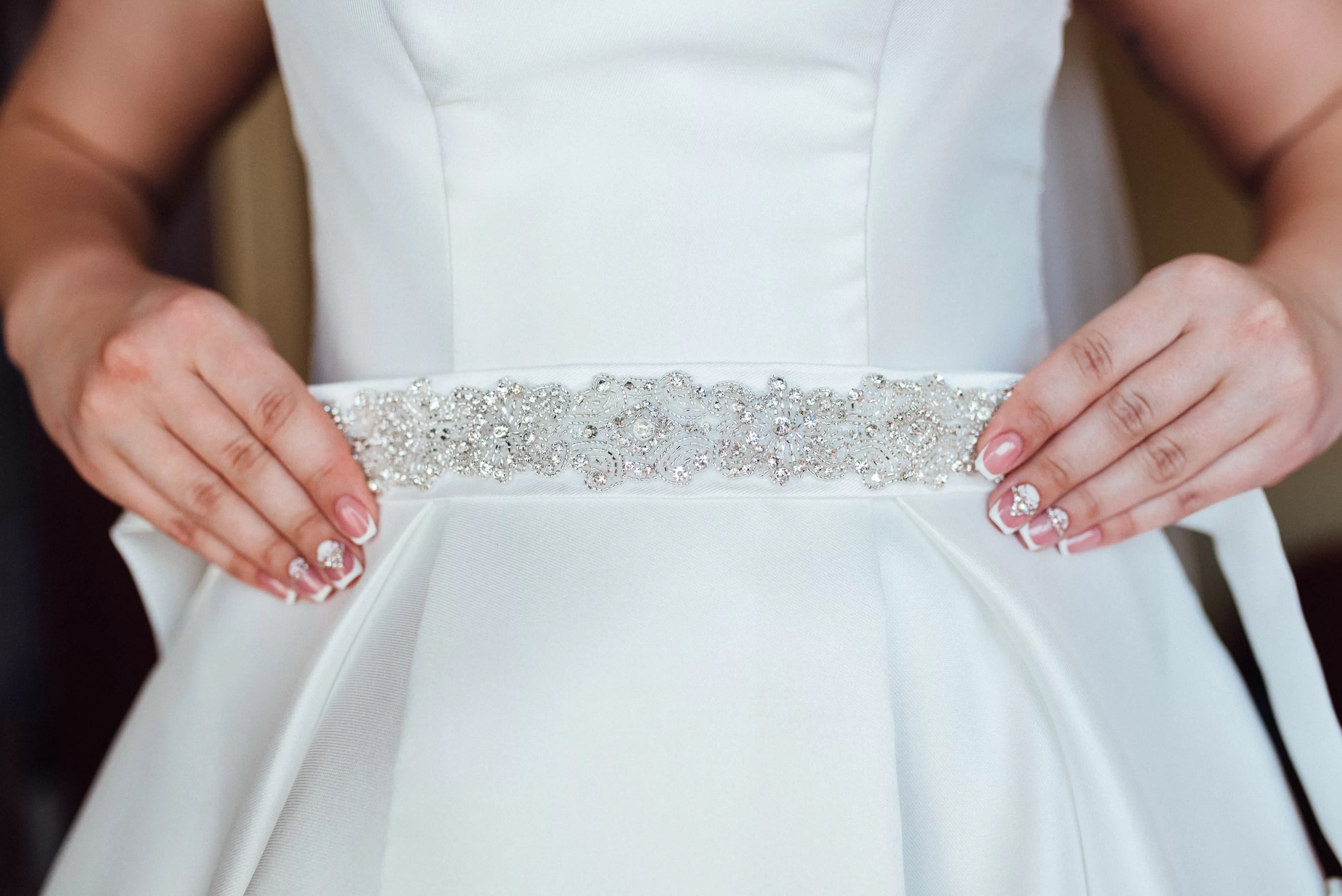 Mulher usando um vestido de noiva branco simples com um cinto brilhante. A foto da foco apenas para a parte da cintura do vestido.