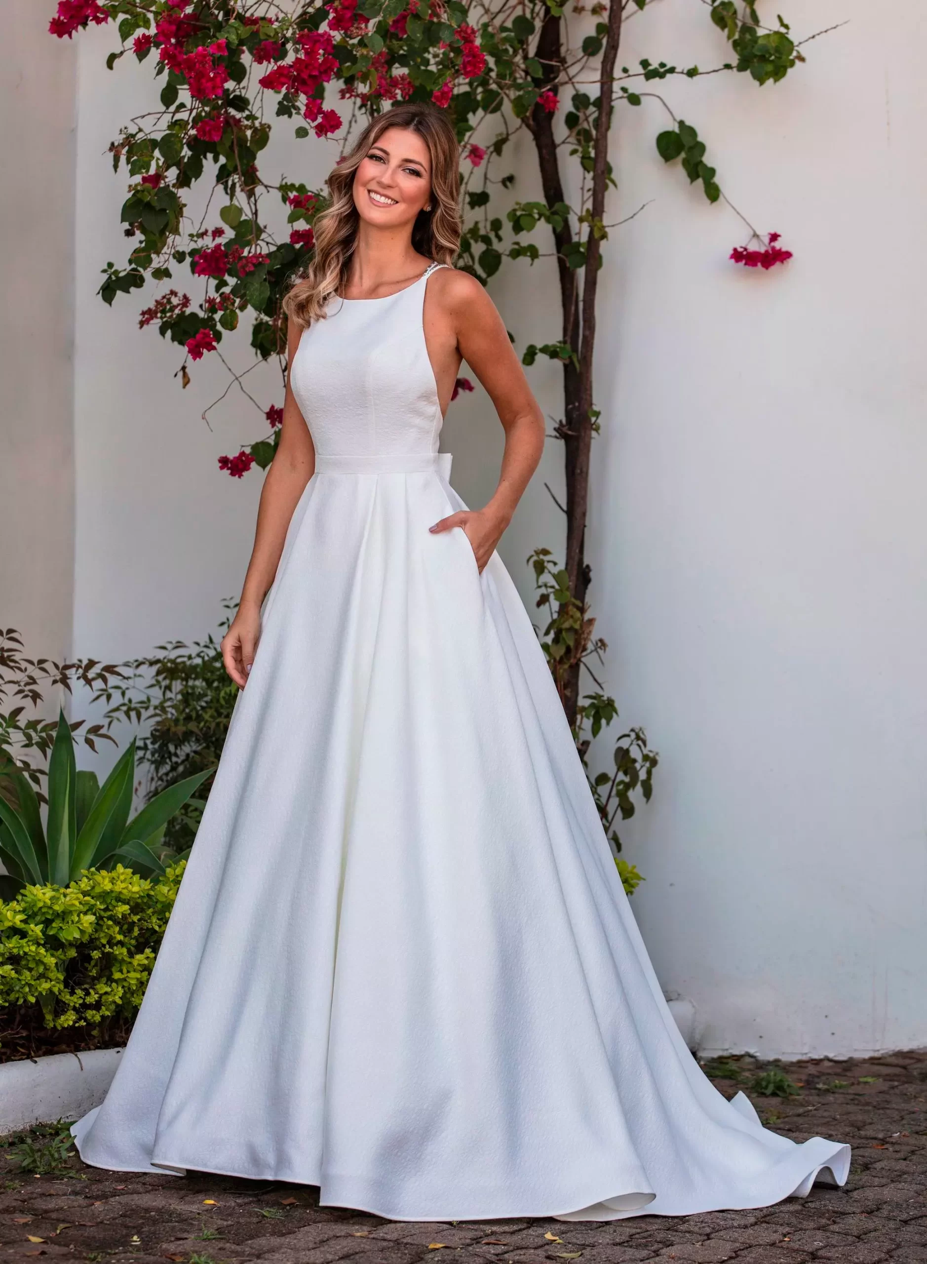 Mulher usando vestido de noiva evase branco e sorrindo para a câmera.