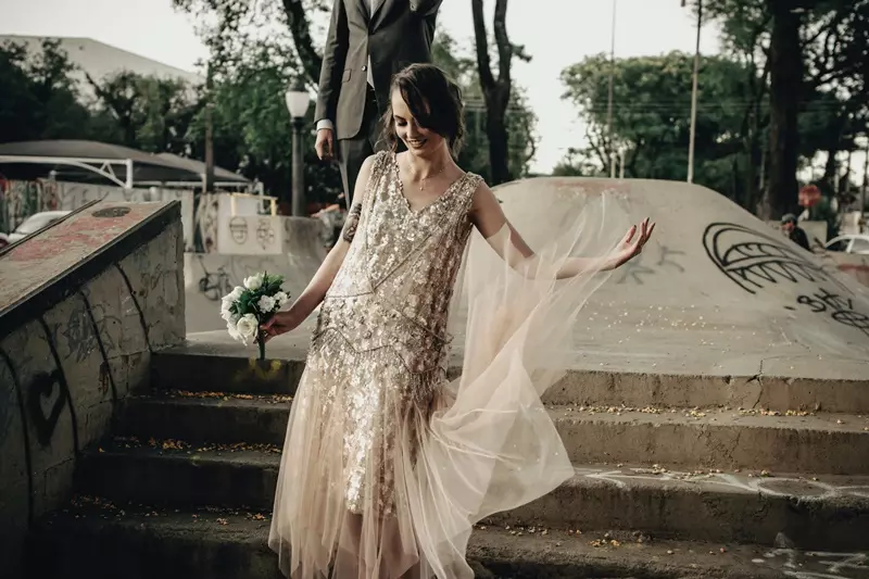 Mulher sorridente usando um vestido de noiva vintage e segurando um buque de flores.