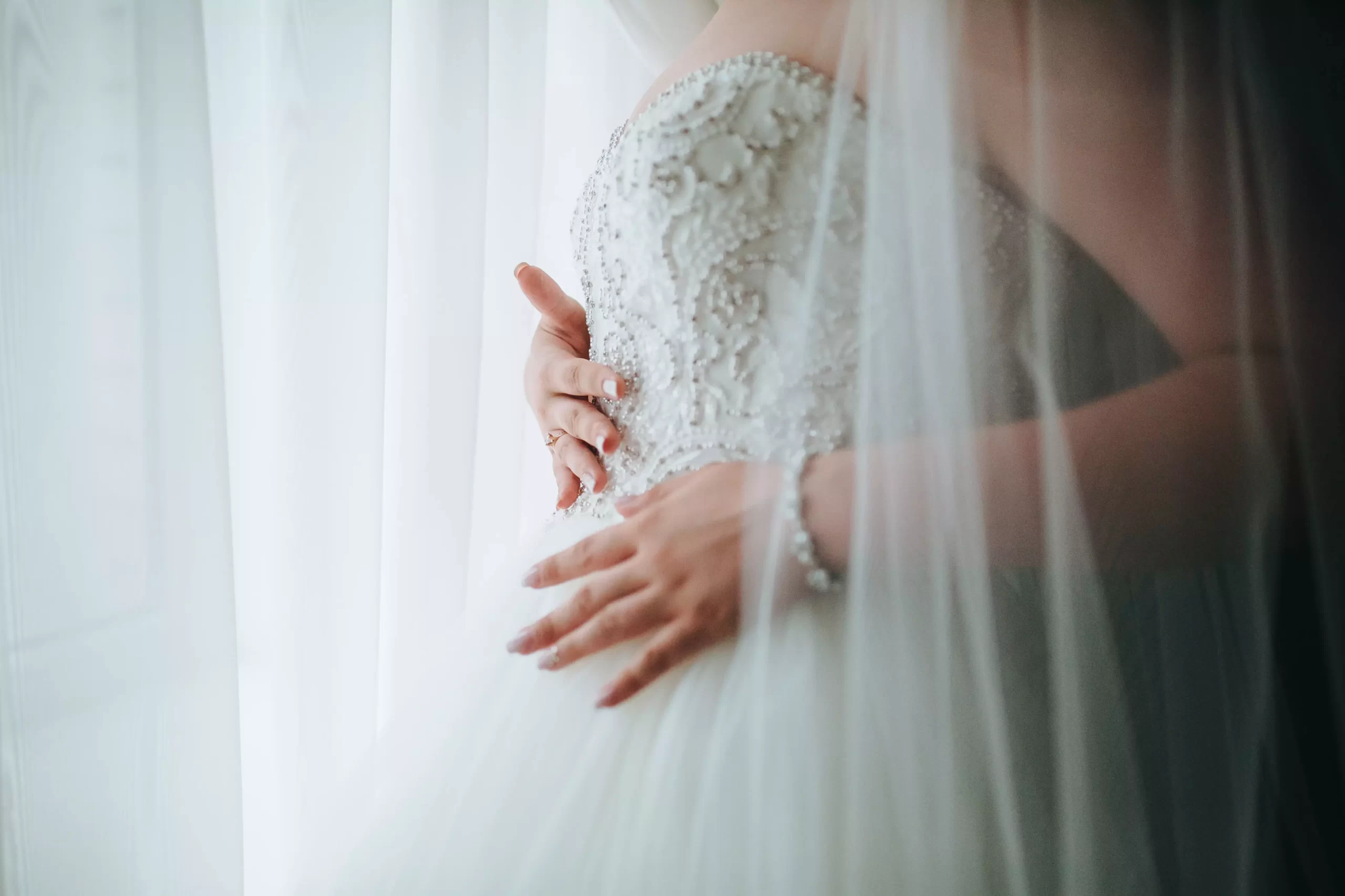 Mulher usando um vestido de noiva com o corpete detalhado. A foto mostra ela passando as mãos nos detalher do corpete.